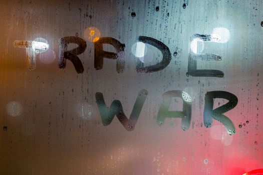 the words trade war written on night wet window glass close-up with blurred background.