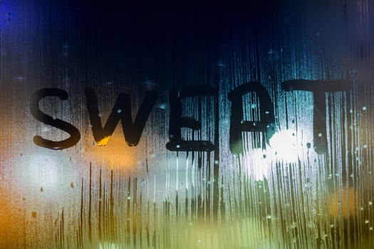 the word sweat written on night wet window glass close-up with bokeh background.