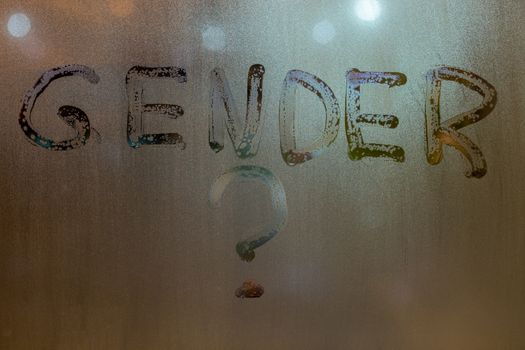 the question gender written by finger on night wet glass with blurred lights in background.