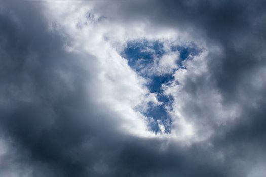 Incoming storm close-up cloudscape at march daylight in continental europe. T-form gap in dence cloud, captured with telephoto lens.