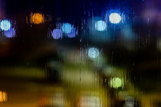 an abstract background night street lights bokeh through wet glass, close-up with selective focus.