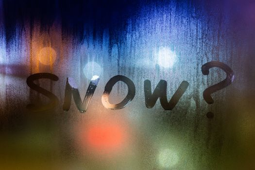 question snow written on night wet window glass close-up with bokeh background.