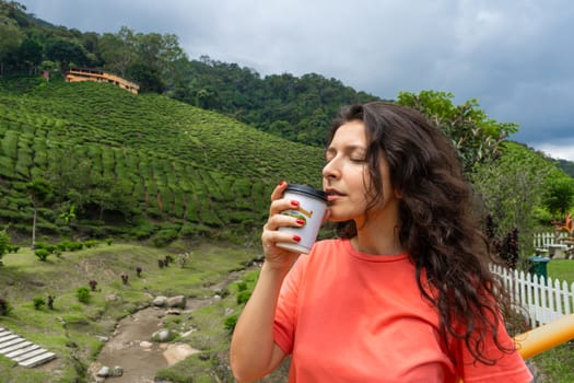 Brunette tourist girl enjoys tea from a craft cup against the background of a green tea valley