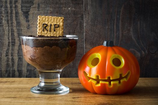 Funny Halloween chocolate mousse with tomb cookie on wooden table