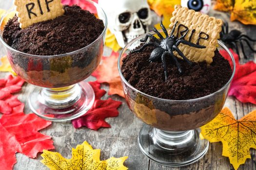 Funny Halloween chocolate mousse with tomb cookie on wooden table