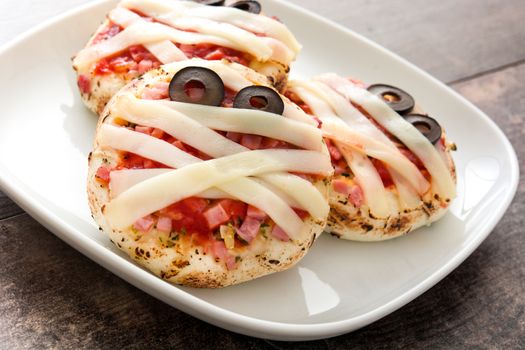 Halloween mummies mini pizzas on wooden table.