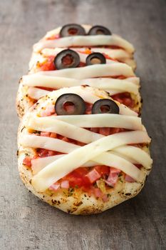 Halloween mummies mini pizzas on wooden table.