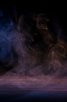 Conceptual image of multi-colored smoke isolated on dark black background and wooden table.