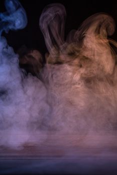 Conceptual image of multi-colored smoke isolated on dark black background and wooden table.