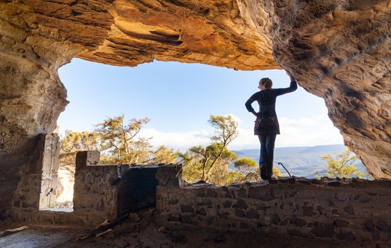 View from inside a cave of a woman looking out to mountain views overlooking Jamison Valley from a cave with a rustic fire pit