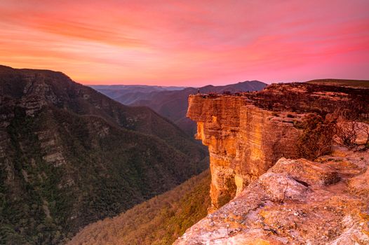 Red sunset over Kanagra Walls located in Kanangra Boyd National Park.  A woman stands on the edge showing the grand scale of the cliffs here catching the last of the golden light