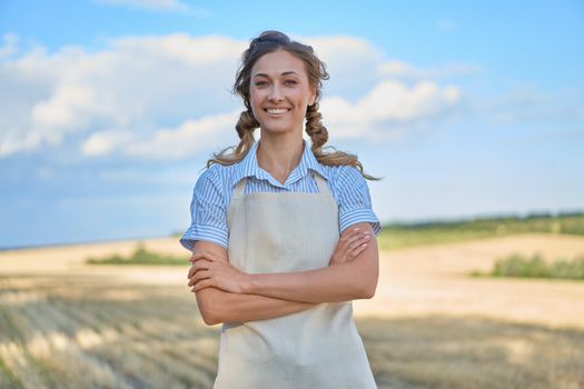 Woman farmer apron standing farmland smiling Female agronomist specialist farming agribusiness Happy positive caucasian worker agricultural field Pretty girl arms crossed cloudy sky background