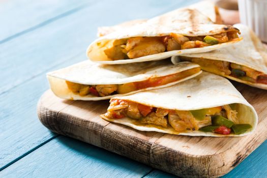 Mexican quesadilla with chicken, cheese and peppers on blue wooden table.