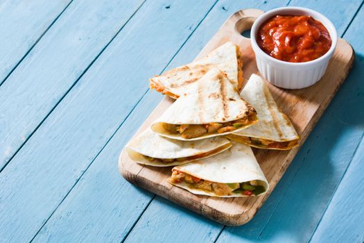 Mexican quesadilla with chicken, cheese and peppers on blue wooden table.