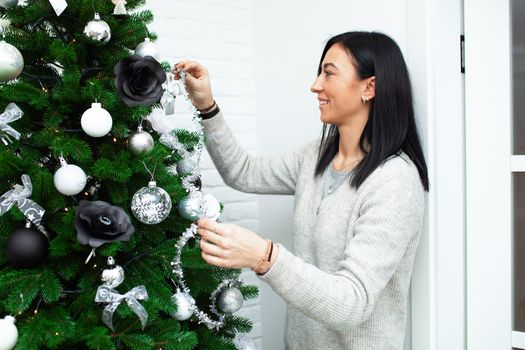 A young woman decorate the Christmas tree, preparing for the New Year's celebration. Female decorate a Christmas tree. Beautiful girl are smiling and have fun during the Christmas holidays.
