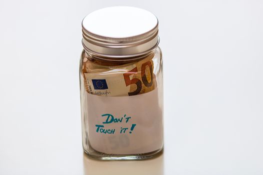 Composition with saving money banknotes in a glass jar with text Do not touch it. Concept of investing and keeping money, close up isolated.