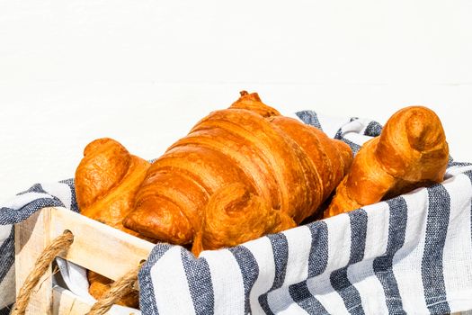 Fresh croissant, puff pastry and buttered french croissant on wooden crate. Food and breakfast concept. Detail of desserts and fresh pastries