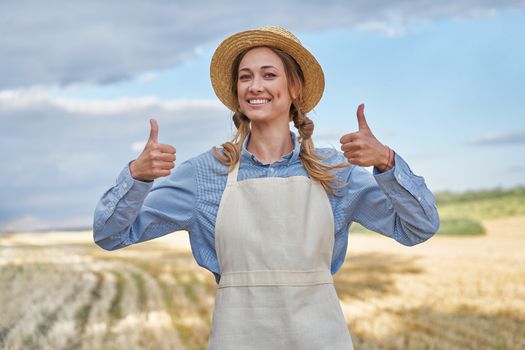 Woman farmer straw hat apron standing farmland smiling showing thumb up sign Female agronomist specialist farming agribusiness Happy positive caucasian worker agricultural field