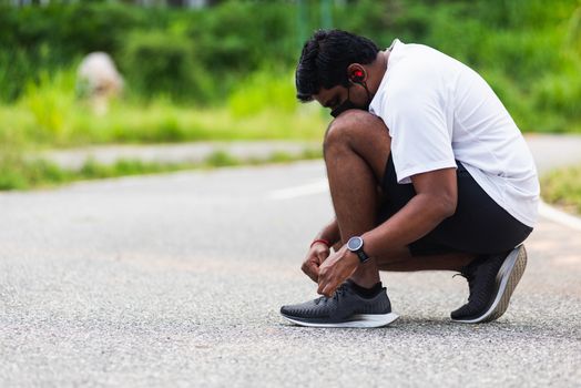 Close up Asian sport runner black man wear watch sitting he trying shoelace running shoes getting ready for jogging and run at the outdoor street health park, healthy exercise workout concept