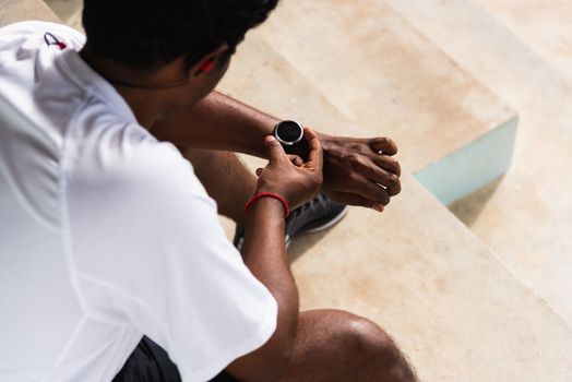Close up Asian young athlete sport runner black man wear modern time smart watch he sitting resting before training running at the outdoor street health park, healthy exercise before workout concept