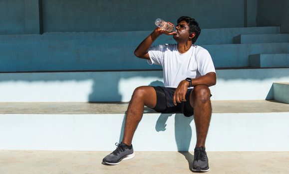 Close up Asian young sport runner black man wear athlete headphones he drinking water from a bottle after running at the outdoor street health park, healthy exercise workout concept