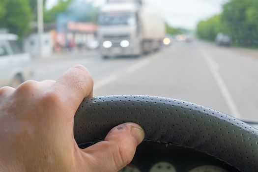 view of the driver hand on the steering wheel of a car against the background of a passing cargo van