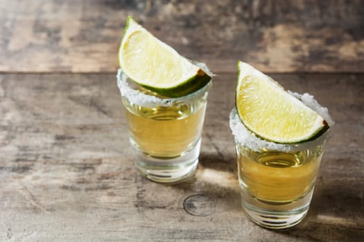 Mexican Gold tequila with lime and salt on wooden table.