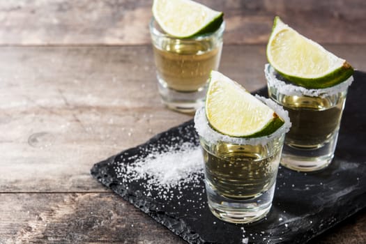 Mexican Gold tequila with lime and salt on wooden table.