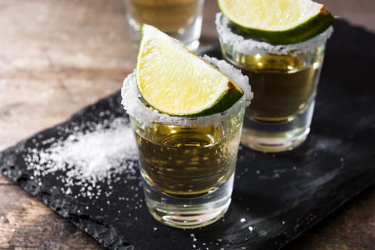 Mexican Gold tequila with lime and salt on wooden table.