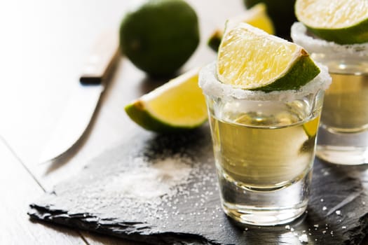 Mexican Gold tequila with lime and salt on wooden table.