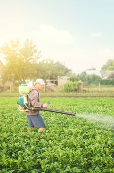 A farmer with a mist sprayer spray treats the potato plantation from pests and fungus infection. Harvest processing. Protection and care. Agriculture and agribusiness. Use chemicals in agriculture.