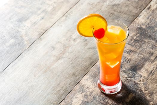 Tequila sunrise cocktail in glass on wooden table.