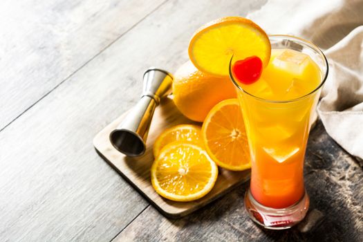 Tequila sunrise cocktail in glass on wooden table.