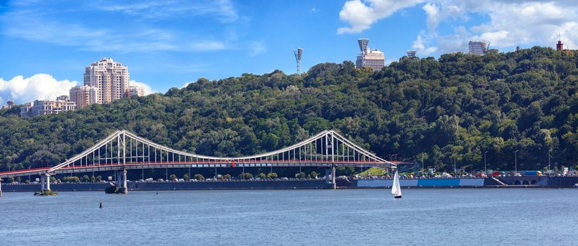 Pedestrian bridge in Kyiv, view panorama of the city of Kyiv, on Dnipro river, sailboat, Ukraine.