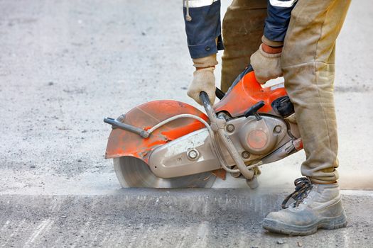 A worker mends part of the road, cuts out worn asphalt in a cloud of dust using a portable concrete cutter and a cutting diamond blade, copy space, close-up.