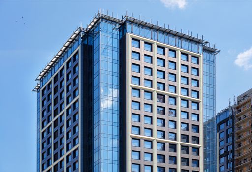 Fragment of the symmetrical facades of modern high-rise residential buildings of glass and concrete, updating the old residential areas of the city, the windows reflect the blue sky and the crane.