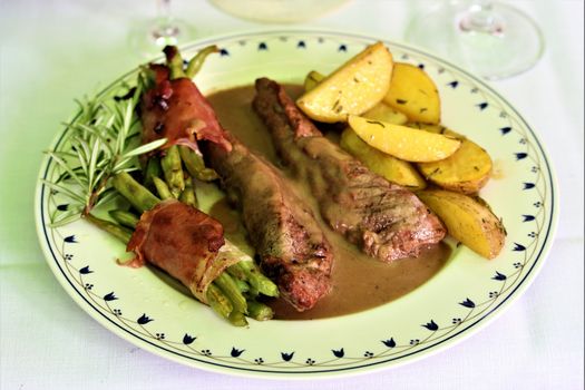 grilled lamb fillet with beans wrapped in bacon and potato wedges on a plate