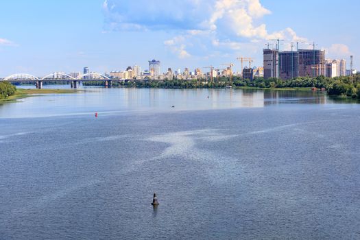 A beautiful cityscape with a view of the Dnipro River in the foreground and new residential areas under construction in the city of Kyiv on the horizon.