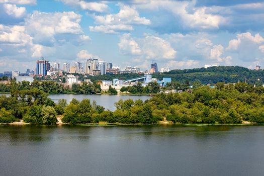 Cityscape of the right bank of Kiev with the Dnieper river and islands in the foreground and a view of a new residential area with high-rise buildings on the horizon on a warm summer day.