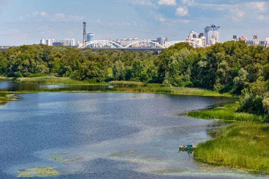 The beautiful bay of the Dnipro with the banks overgrown with reeds, a fishing boat moored to the shore, and on the horizon is the city industry and the landscape of Kyiv.