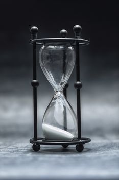 Hourglass with white sand against dark background closeup