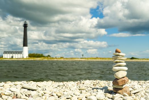 Stones balance, hierarchy stack over blue sea with lighthouse at background. Well-being, freedom and stability concept on Saaremaa Island, Estonia, sorve lighthouse