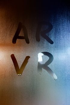 the words ar - fugmented reality - and vr - virtual reality - written by finger on wet glass with blurred street lights background