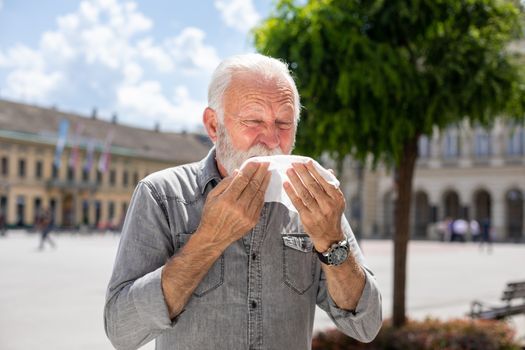 Old man coughs and sneezes into a handkerchief on street, outdoor, hot summer, allergies and illness concept