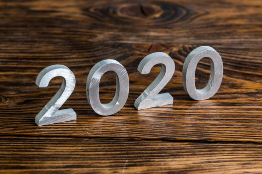 a number 2020 with white metal digits on dark brown wood background with selective focus.