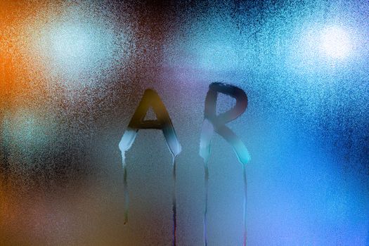 the word ar - augmented reality - written by finger on wet glass with blurred lights in background.