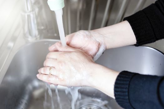 a young Caucasian woman rinses her hands after washing them with soap. Personal hygiene and virus prevention.