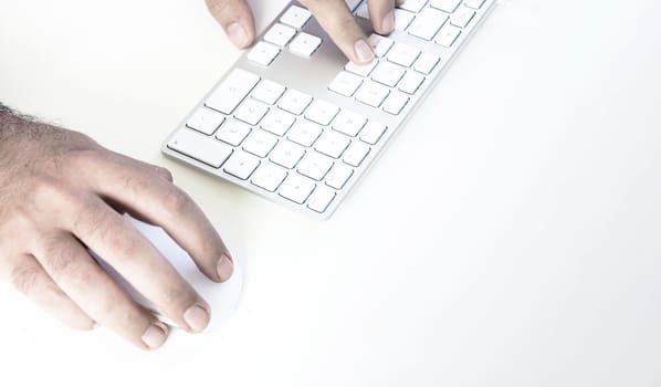 male hand clicking on a mouse and typing on a white keyboard on a white table. White background.