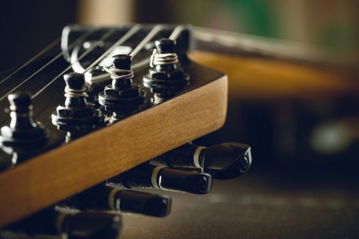 Closeup tuning key on the headstock of the black electric guitar in dark background and morning light. Copy space on the right. Concept of good memory About retro musical instruments and rock music.