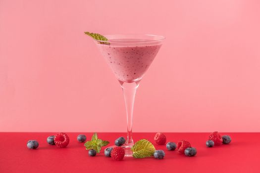 Berry smoothie cup with several blueberries and raspberries on a red and pink background. Minimalist image.